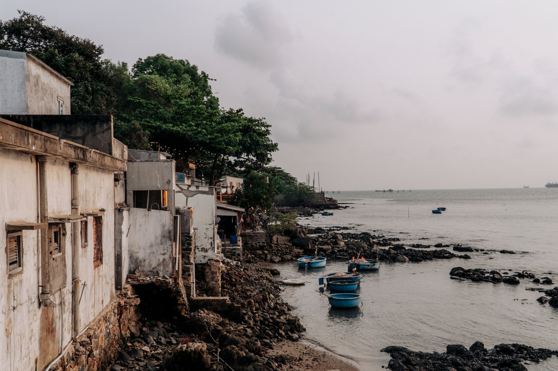 Rustic coastal village in Vũng Tàu, Vietnam, with old buildings and small fishing boats along the rocky shore.